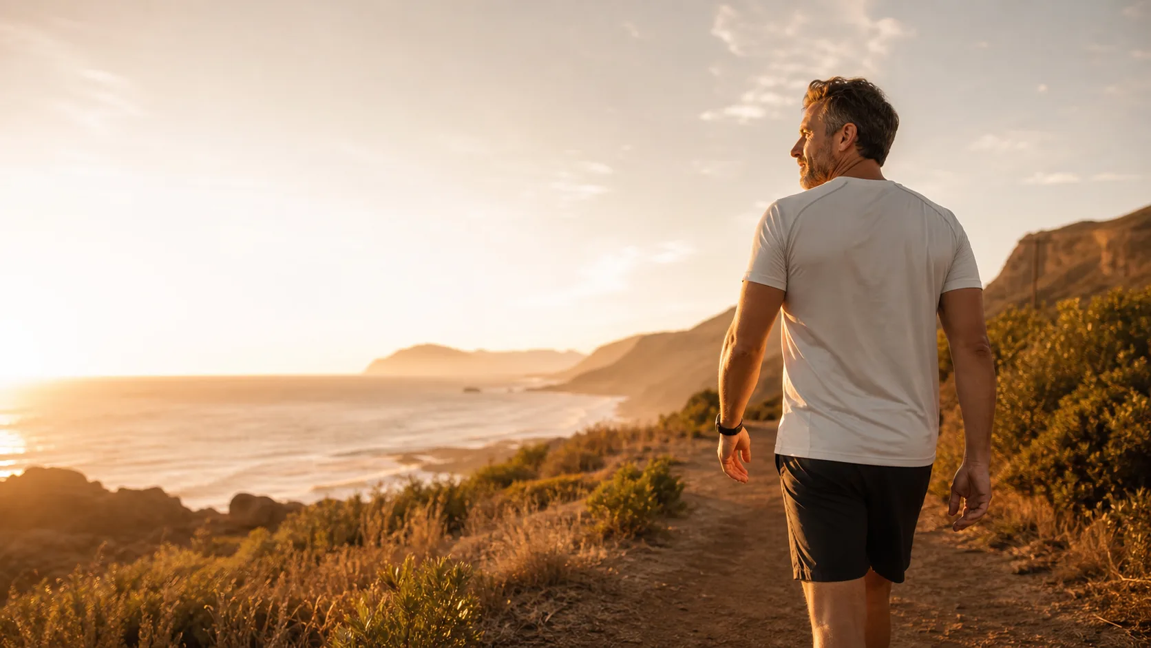 Man walking along a sunlit coastal path at golden hour